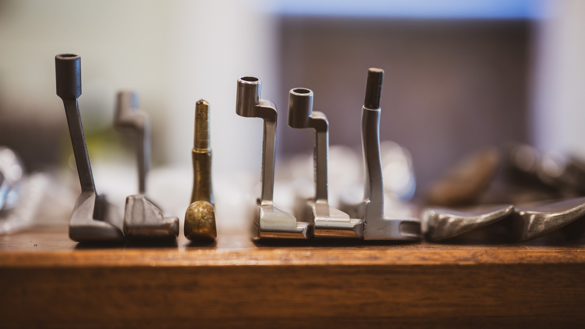 A row of unshafted putter heads standing on a timber shelf, one of them brass