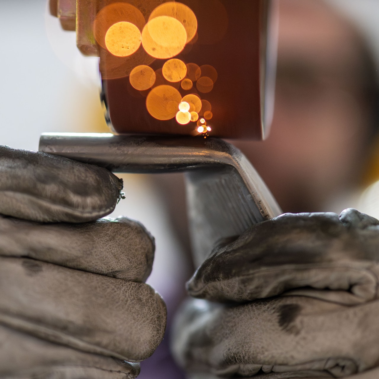 Gloved hands press an iron head to a grinding wheel, sparks glowing orange