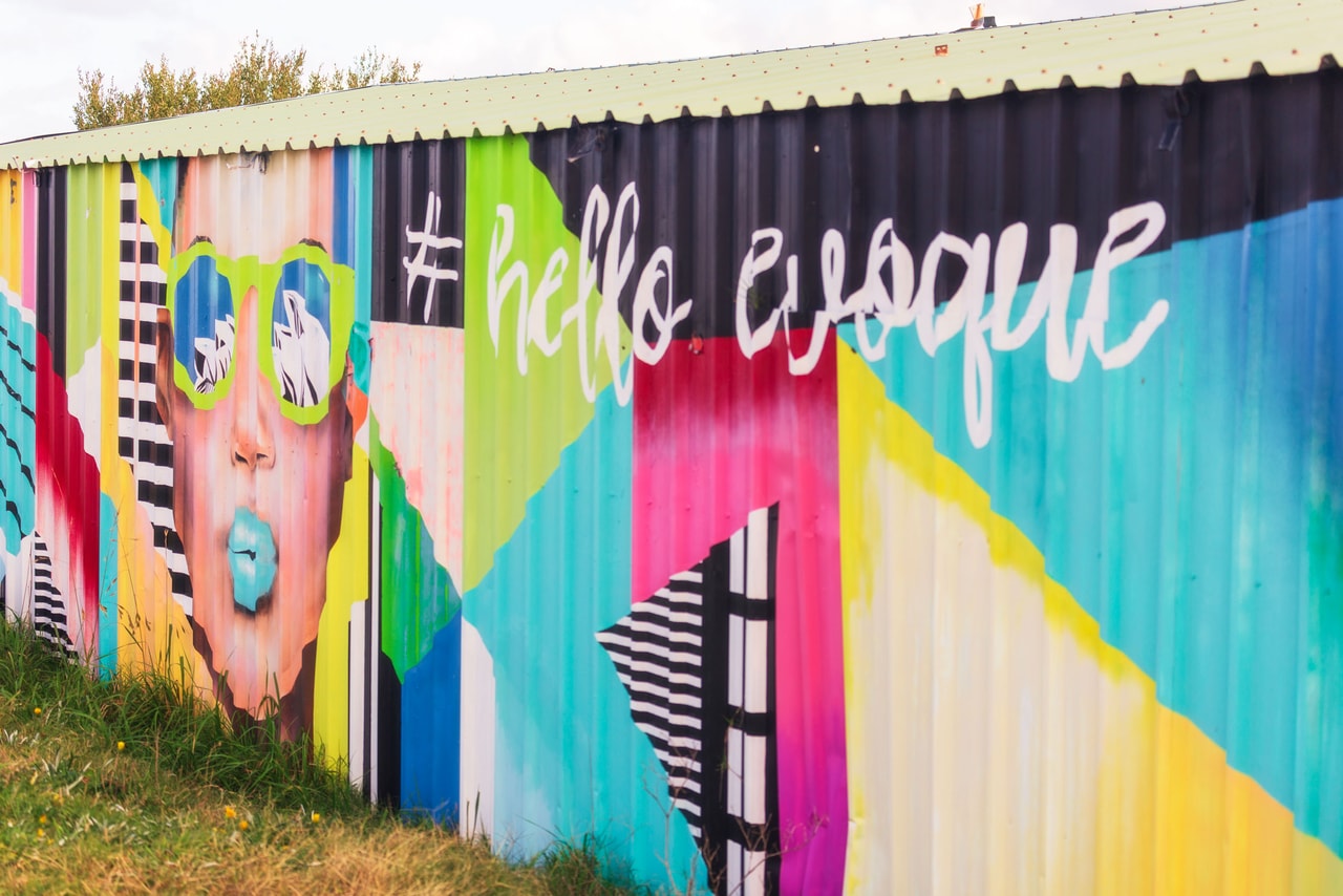 A bright mural on a corrugated shed: a woman in green sunglasses blowing a bubble, ‘#hello evoque’