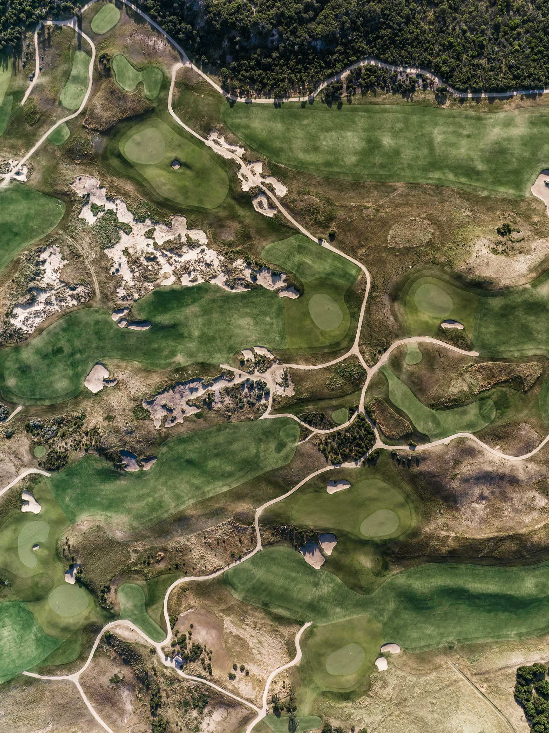 Looking straight down on fairways, greens and sandy scrapes threaded by cart paths through coastal scrub