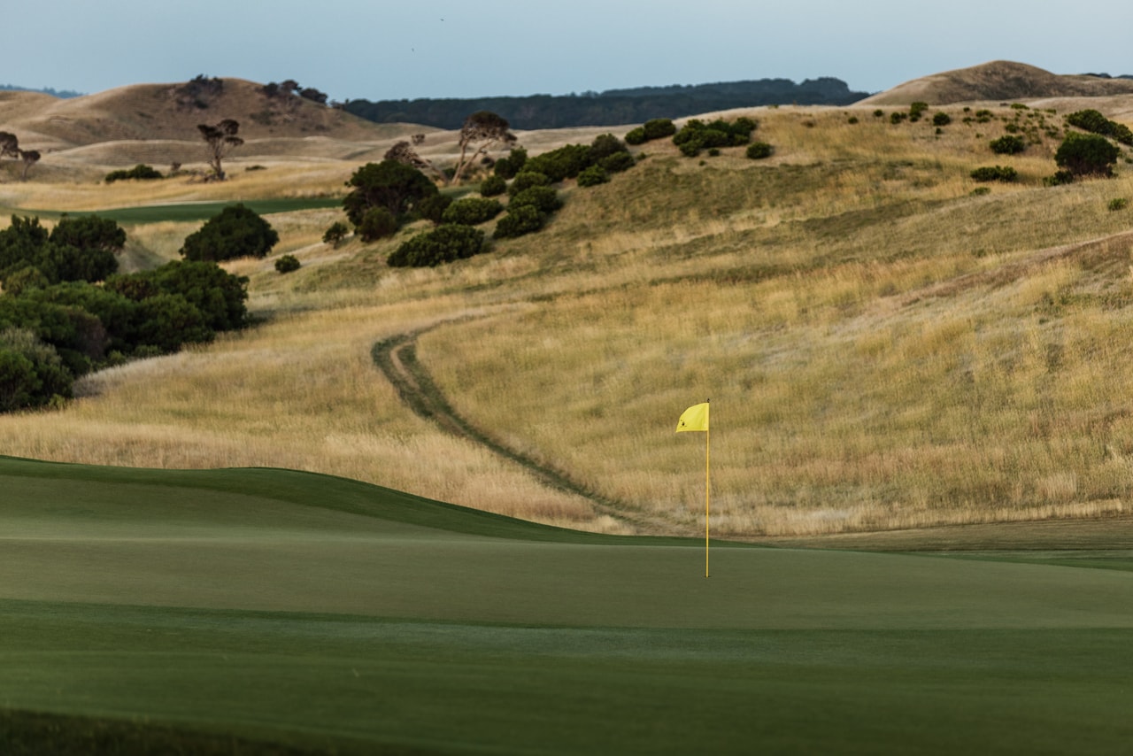 A green and its yellow flag below a slope of golden grass, a track winding up through the scrub