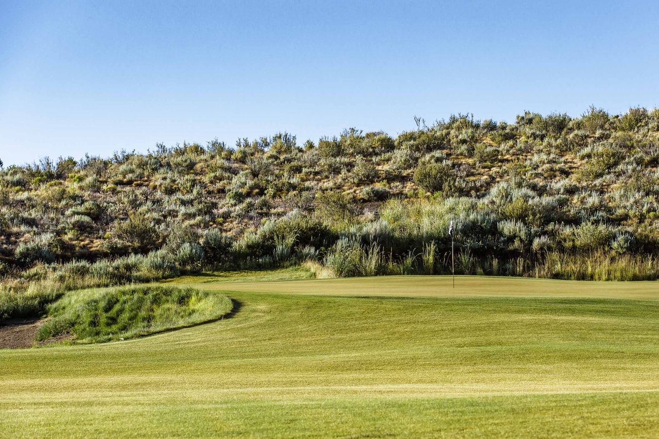 A green and its flag below a hillside of sagebrush, a grassy mound and a bunker to the left