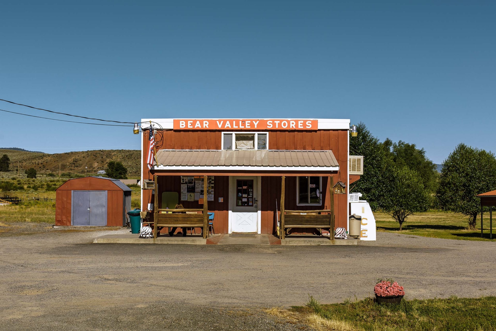 A red weatherboard store under a sign reading ‘Bear Valley Stores’, benches on its porch and a gravel forecourt