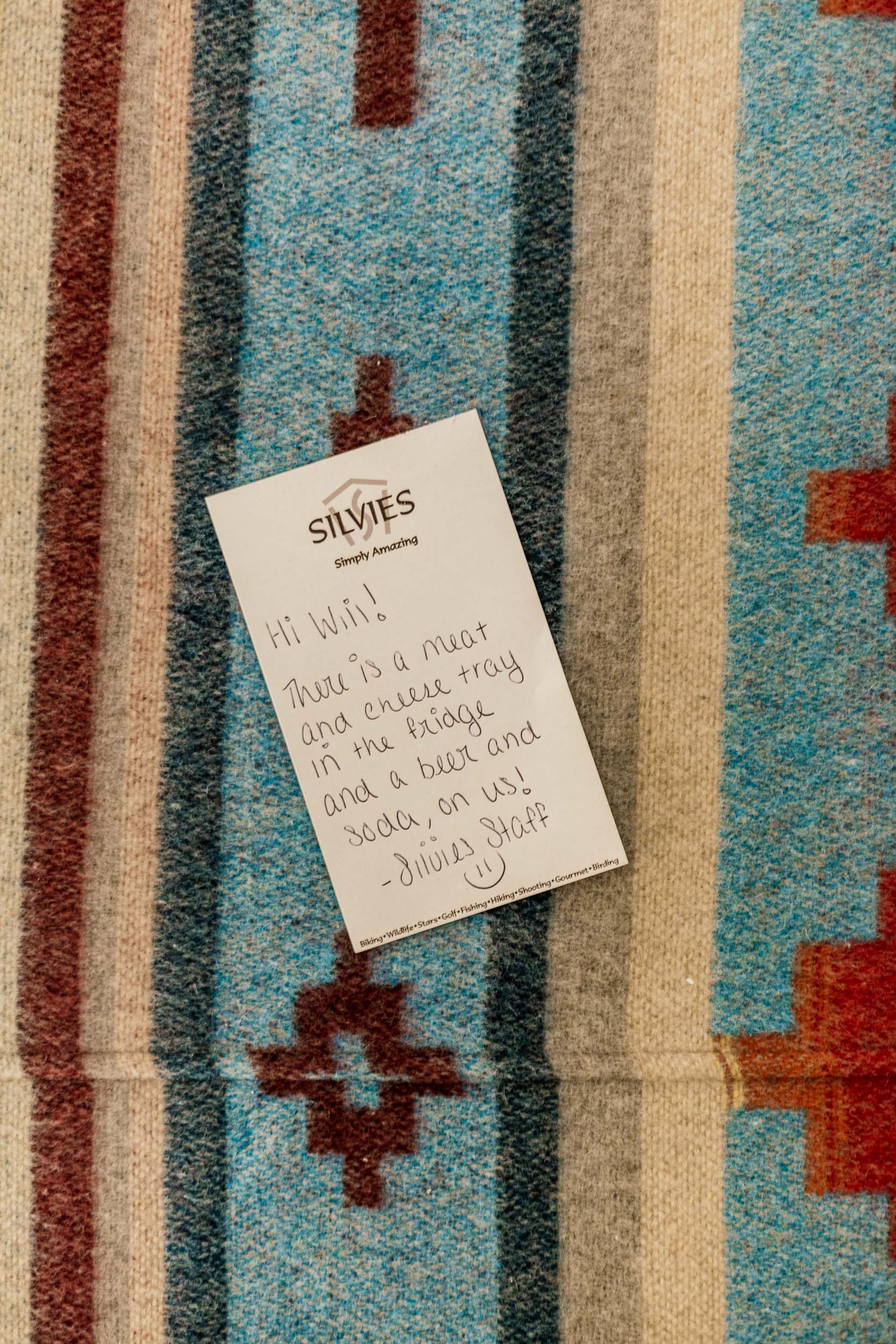 A handwritten Silvies welcome card on a striped wool blanket: a meat and cheese tray and a beer in the fridge